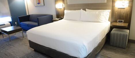 A hotel room with a large bed, a desk, a chair, and a small trash bin.