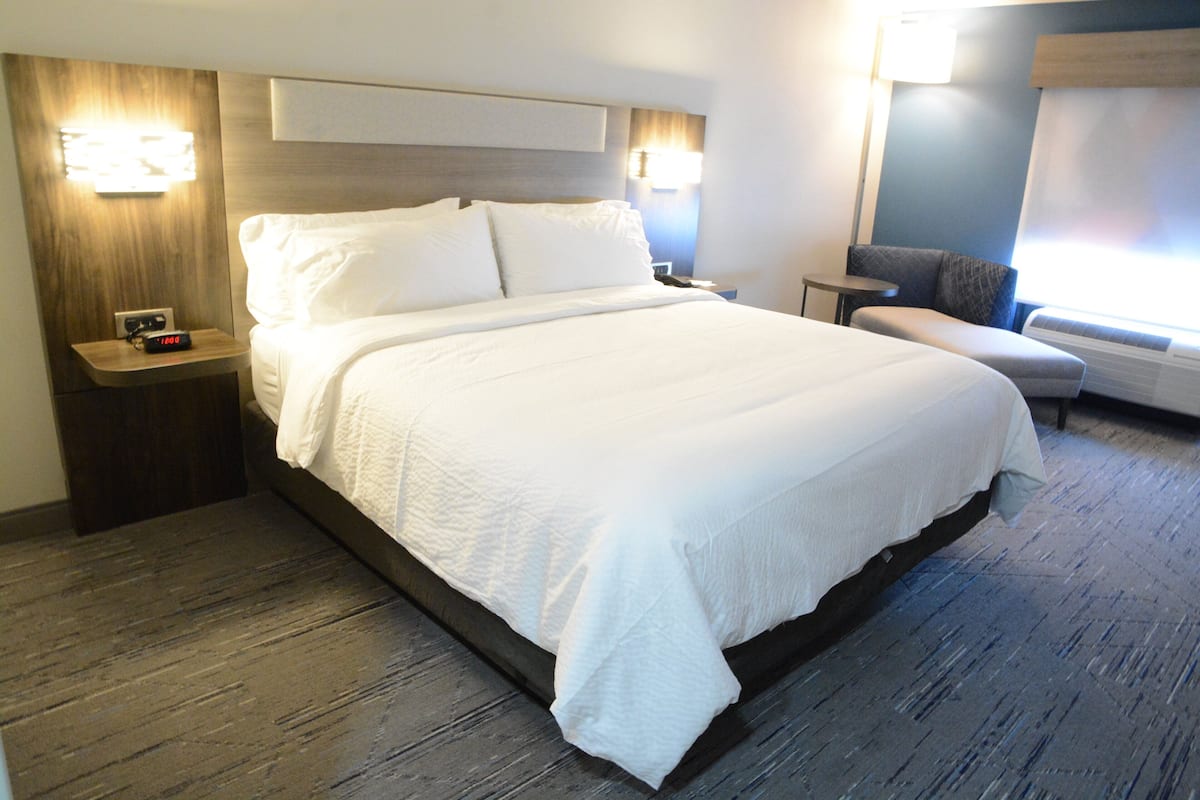 Une chambre d’hôtel avec un grand lit, des tables de chevet, une chaise et une petite table de nuit avec une horloge.