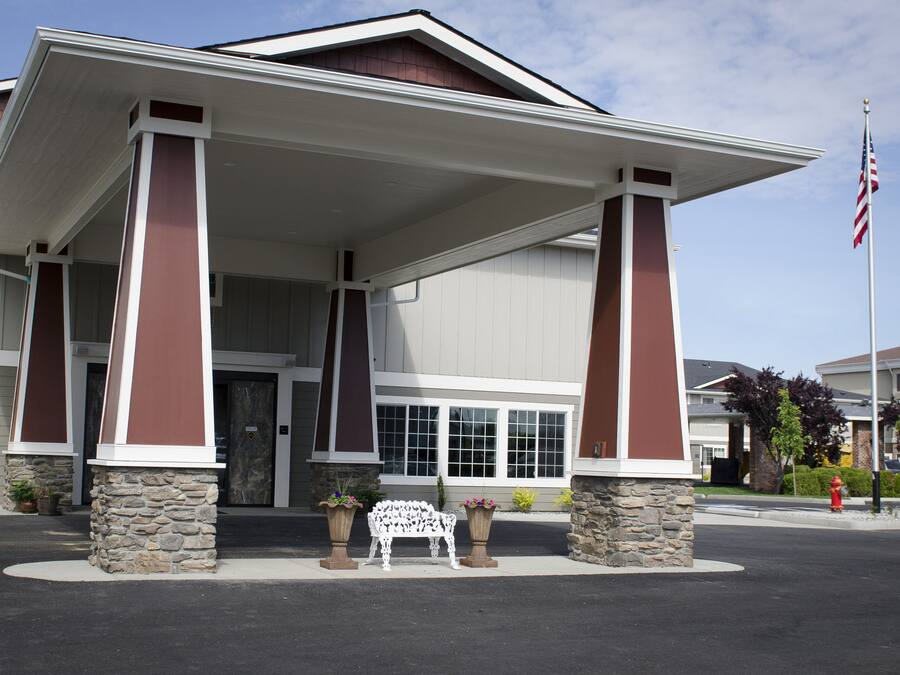 A building with a covered entrance, stone pillars, and a bench with potted plants.