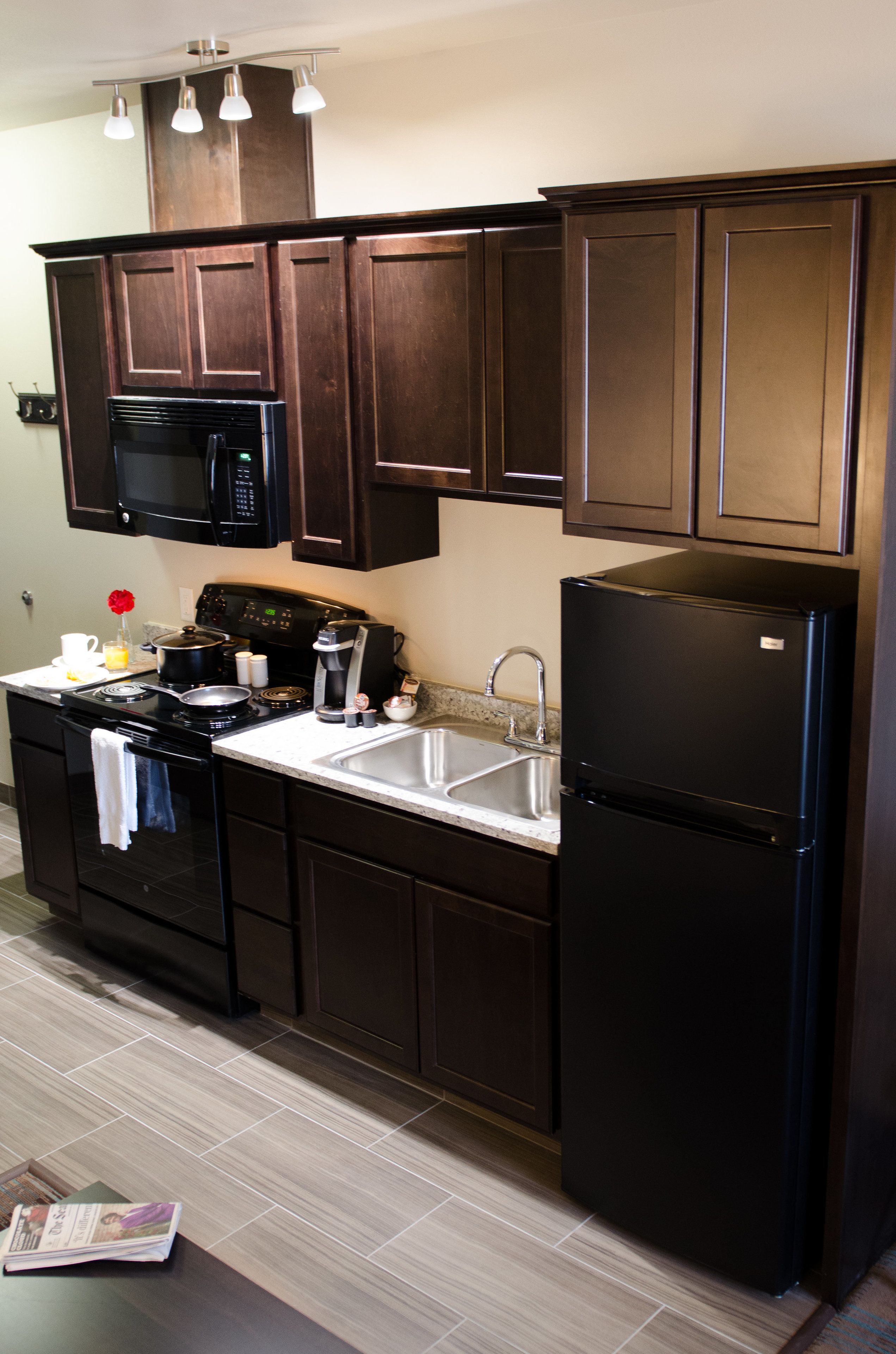 A kitchen with dark wooden cabinets, a black refrigerator, a microwave, and a stove.