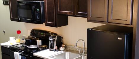 A kitchen with dark wooden cabinets, a black refrigerator, a microwave, and a stove.