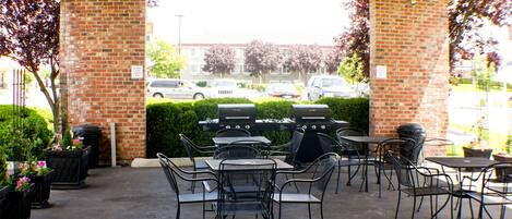An outdoor patio with brick walls, metal tables and chairs, and a grill.
