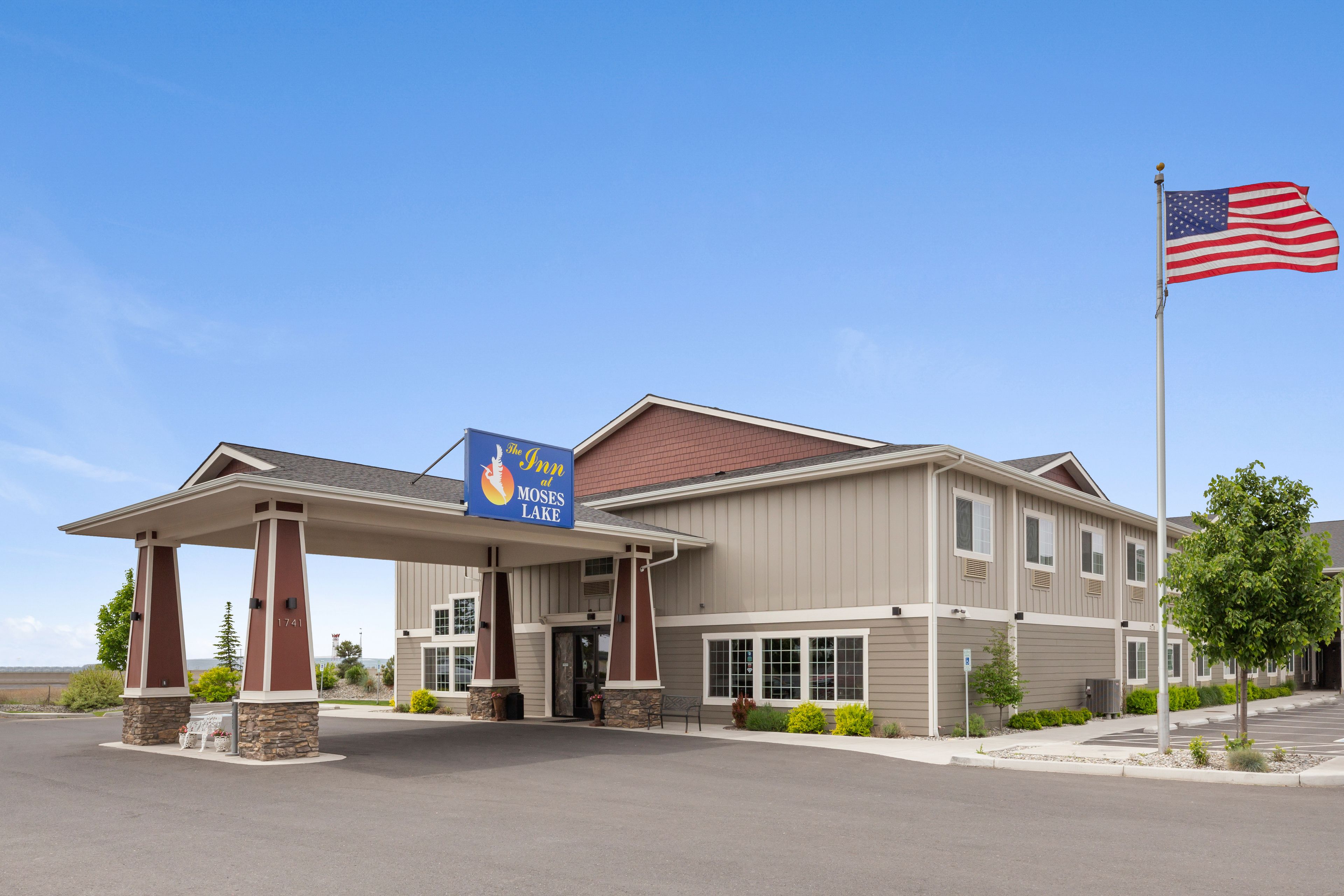 Un hotel con ingresso coperto, un'asta con bandiera americana e un cartello con la scritta 'The Inn at Moses Lake'.