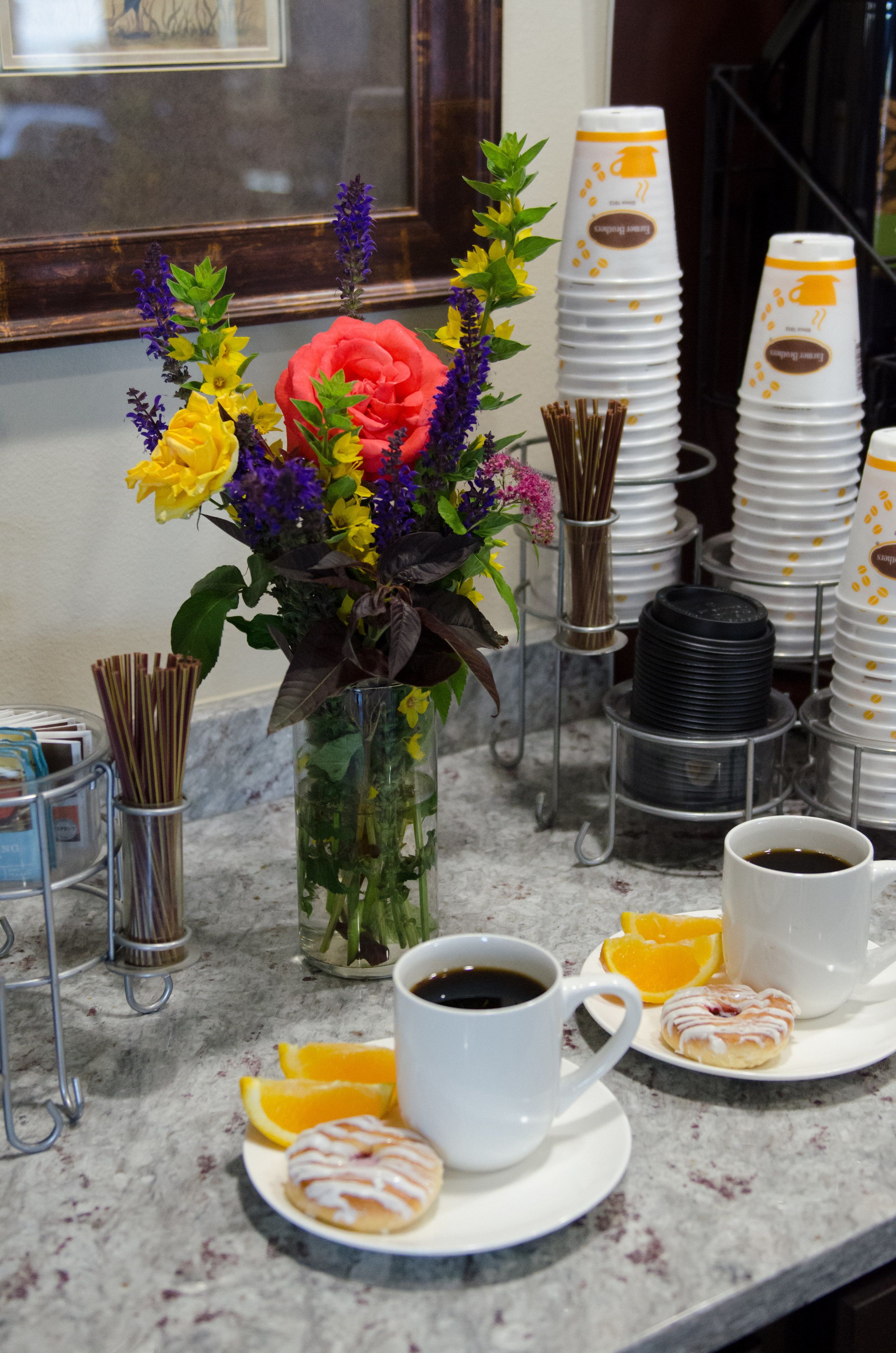 A breakfast setup with coffee cups, orange slices, and pastries on a marble countertop.