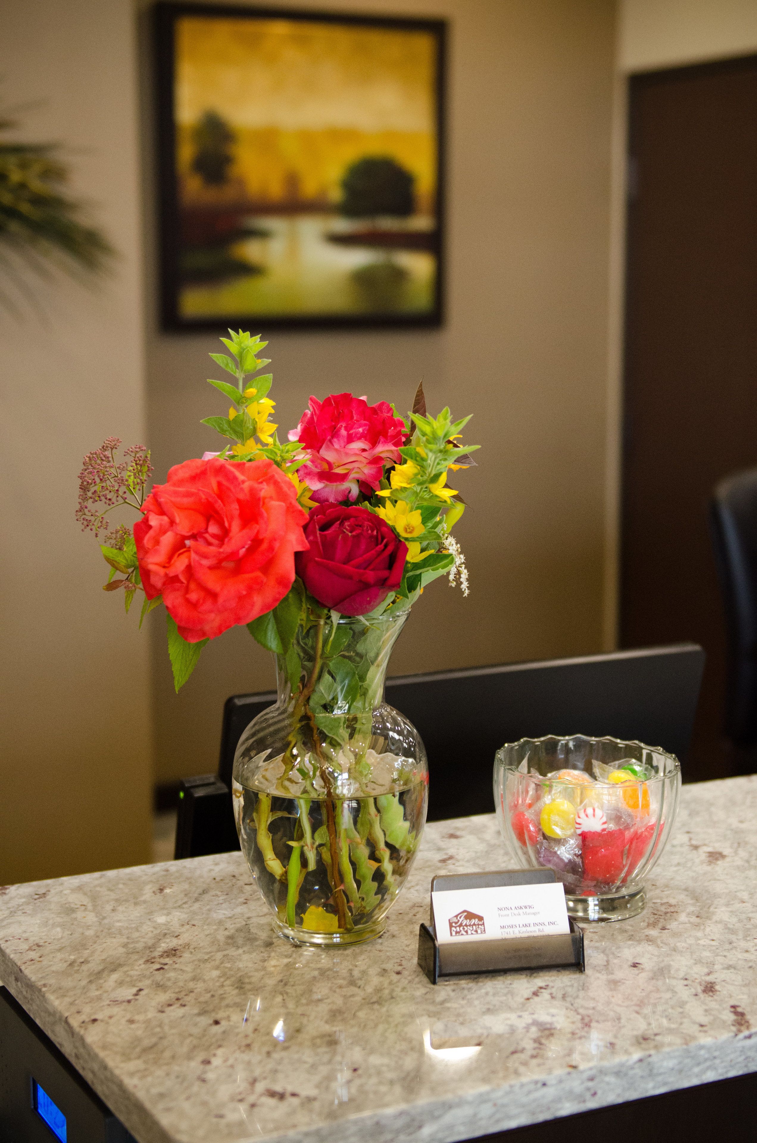 A table with a vase of flowers, a glass bowl with fruit, and a business card.