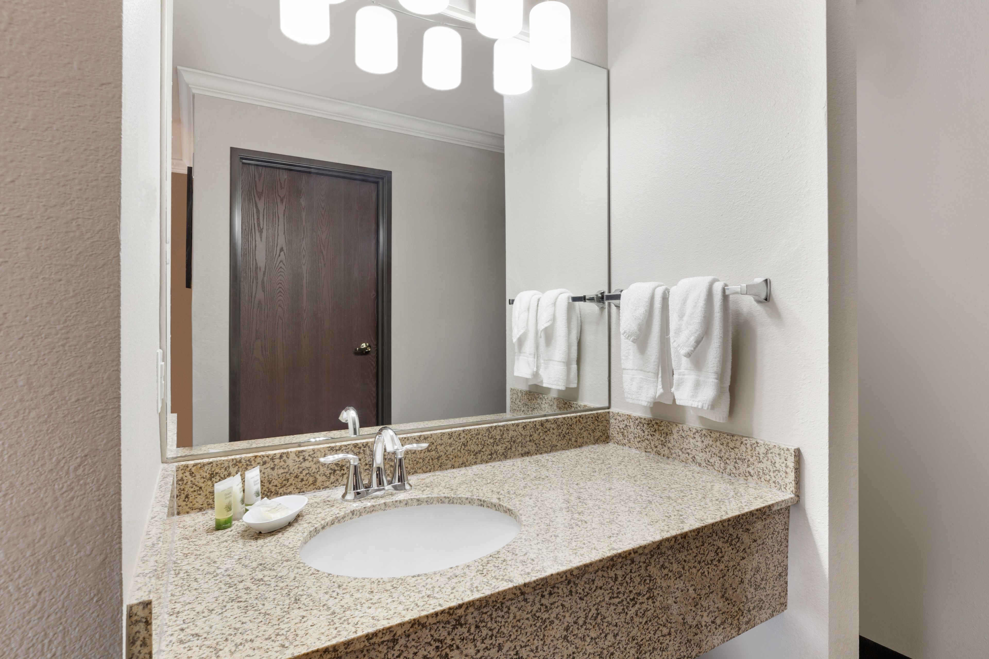 A bathroom with a granite countertop, a white sink, a mirror, and a towel rack.