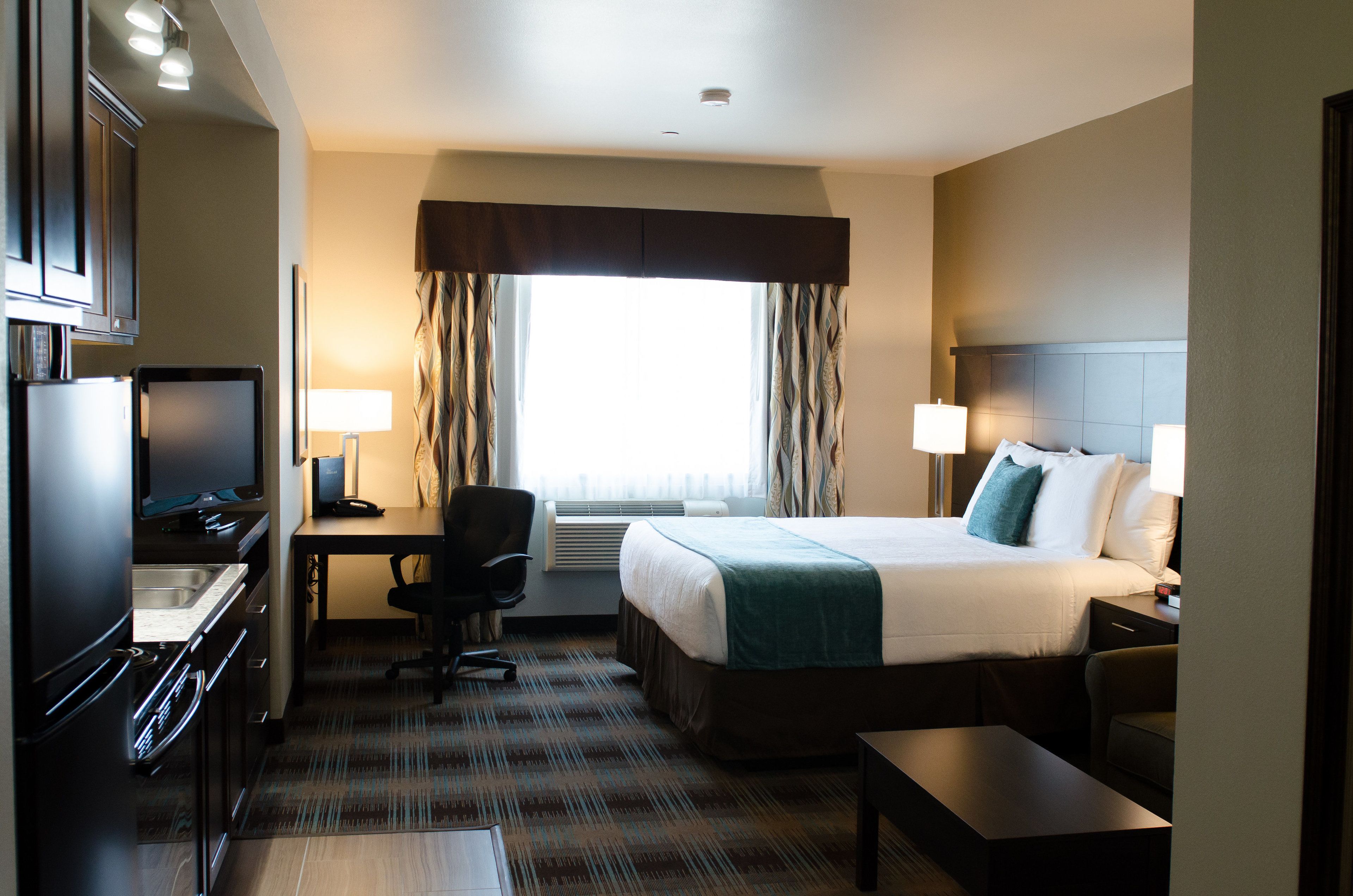 A hotel room with a bed, desk, chair, and kitchenette.