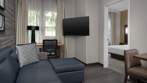 A modern hotel room with a sectional sofa, a desk, a flat-screen TV, a bed, and a view of greenery outside. - Residence Inn by Marriott Arundel Mills BWI Airport (Hanover)