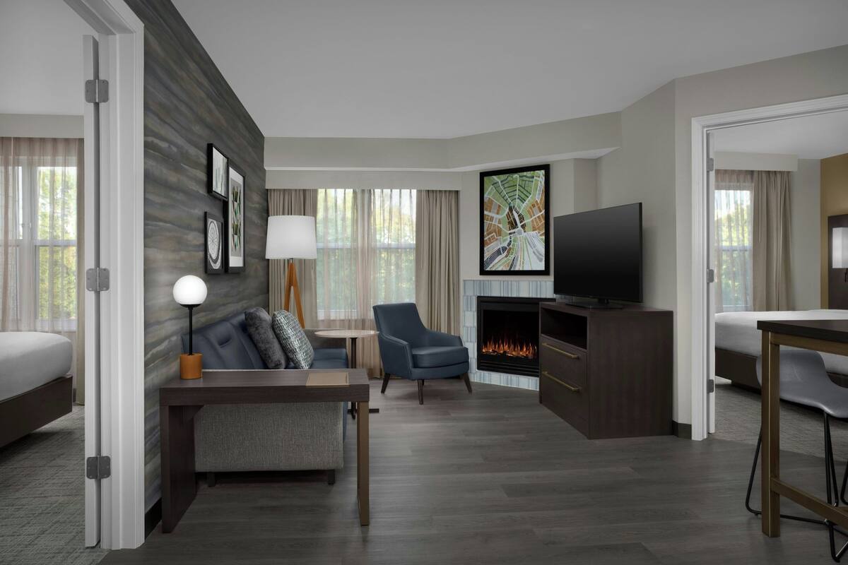 Een hotelkamer met een bed, een bureau, een stoel, een televisie, een open haard en kunstwerken aan de muur.