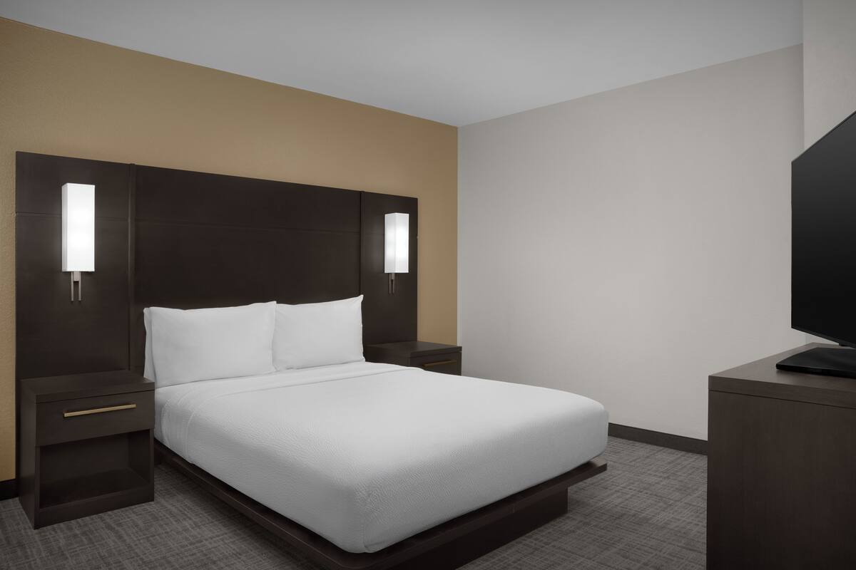 Een hotelkamer met een bed, nachtkastjes, een televisie en wandlampen.