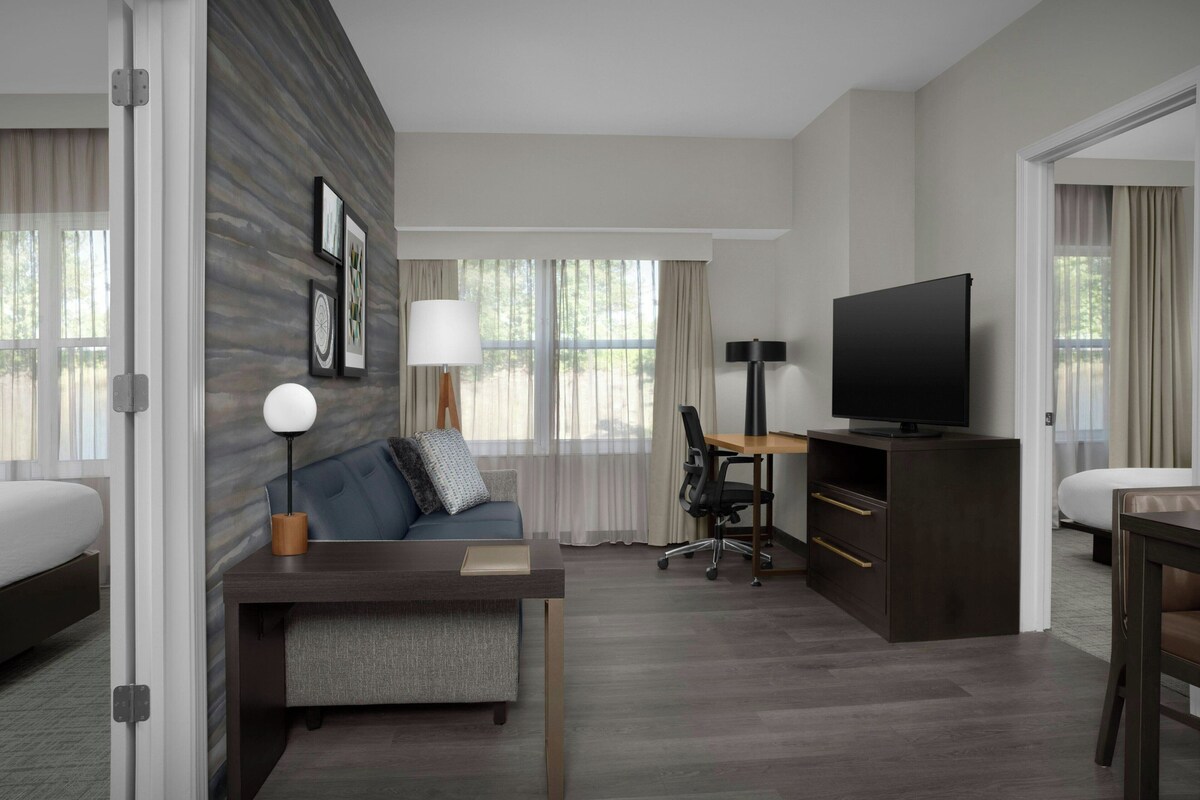 A hotel room with a bed, a desk with a computer, a TV, and a sofa.