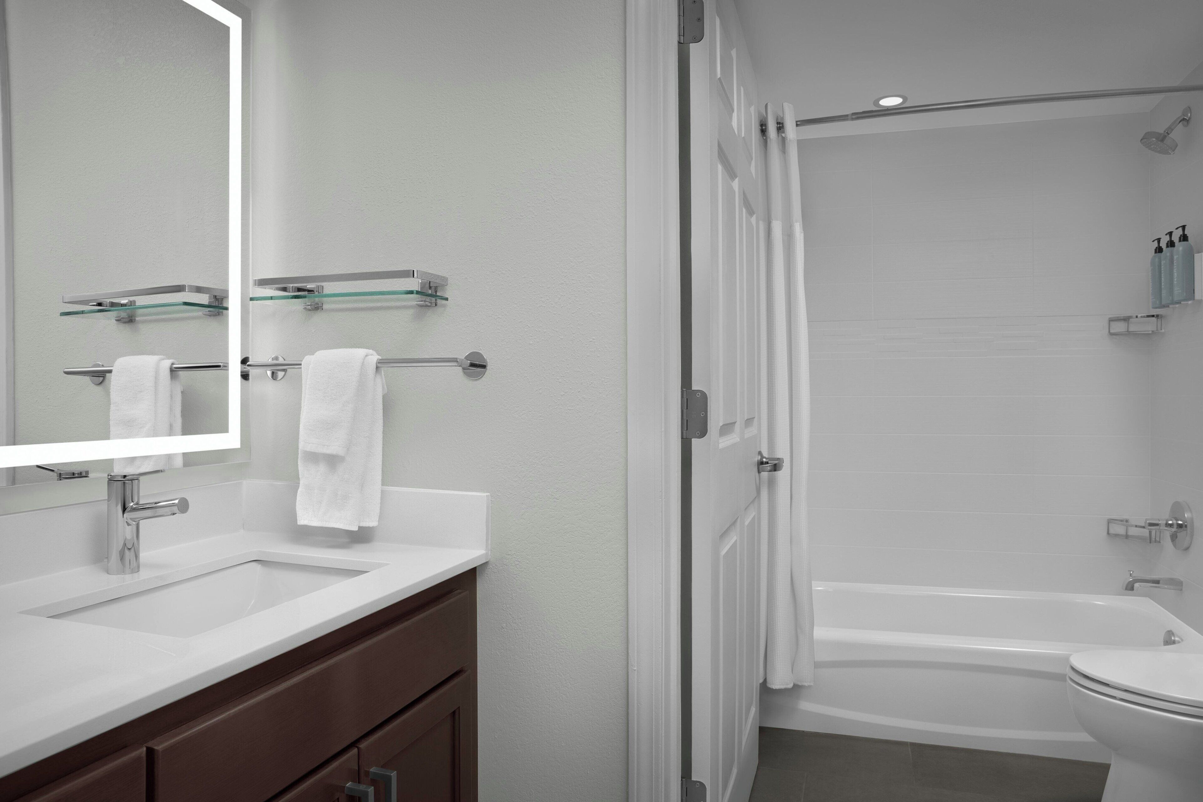 Un baño moderno con un lavamanos, espejo y bañera blancos.