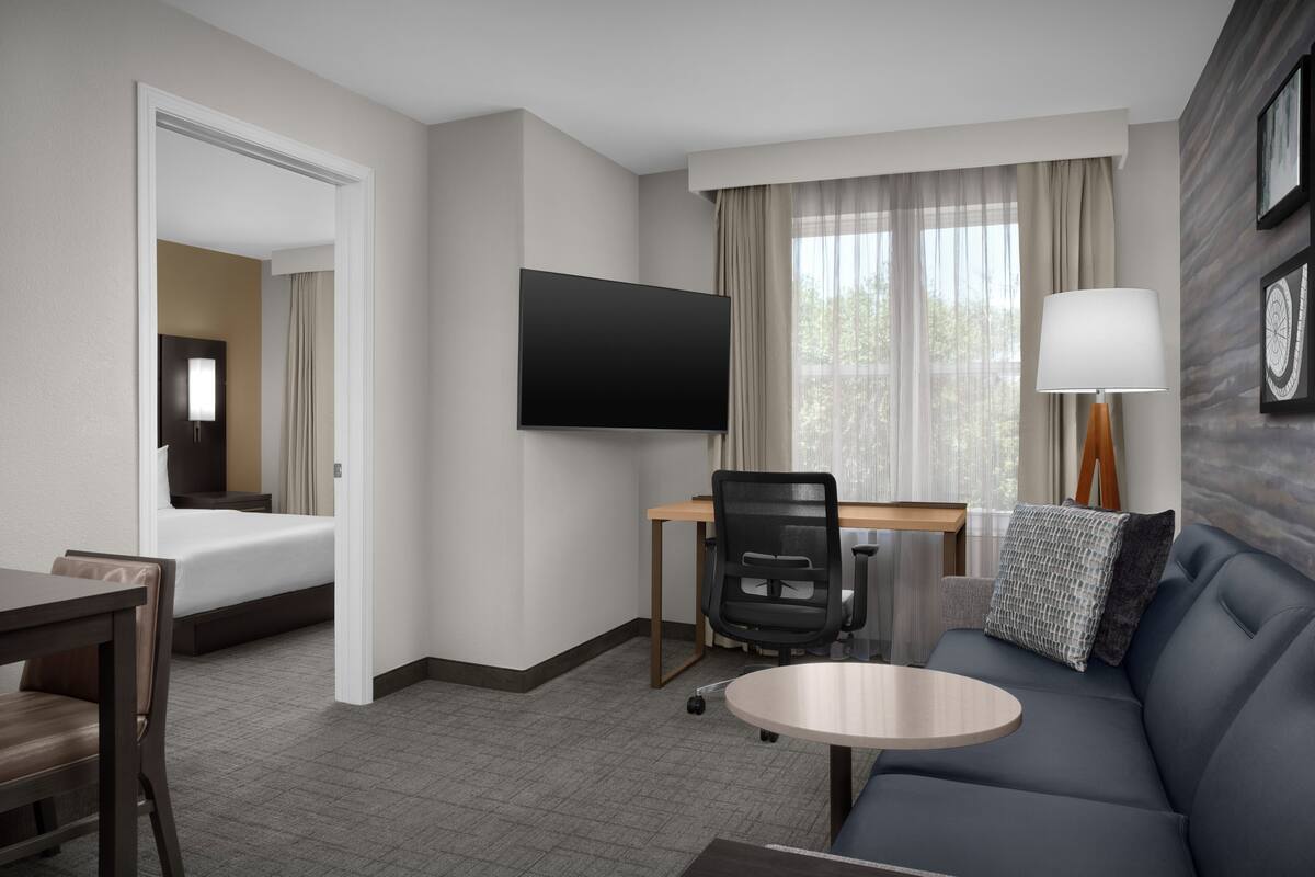 Een hotelkamer met een bed, bureau, stoel, bank, televisie en raam met gordijnen.