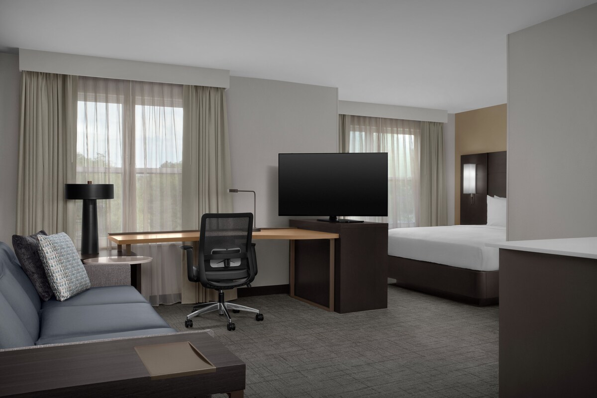 A hotel room with a bed, a desk with a television, a sofa, and a chair.