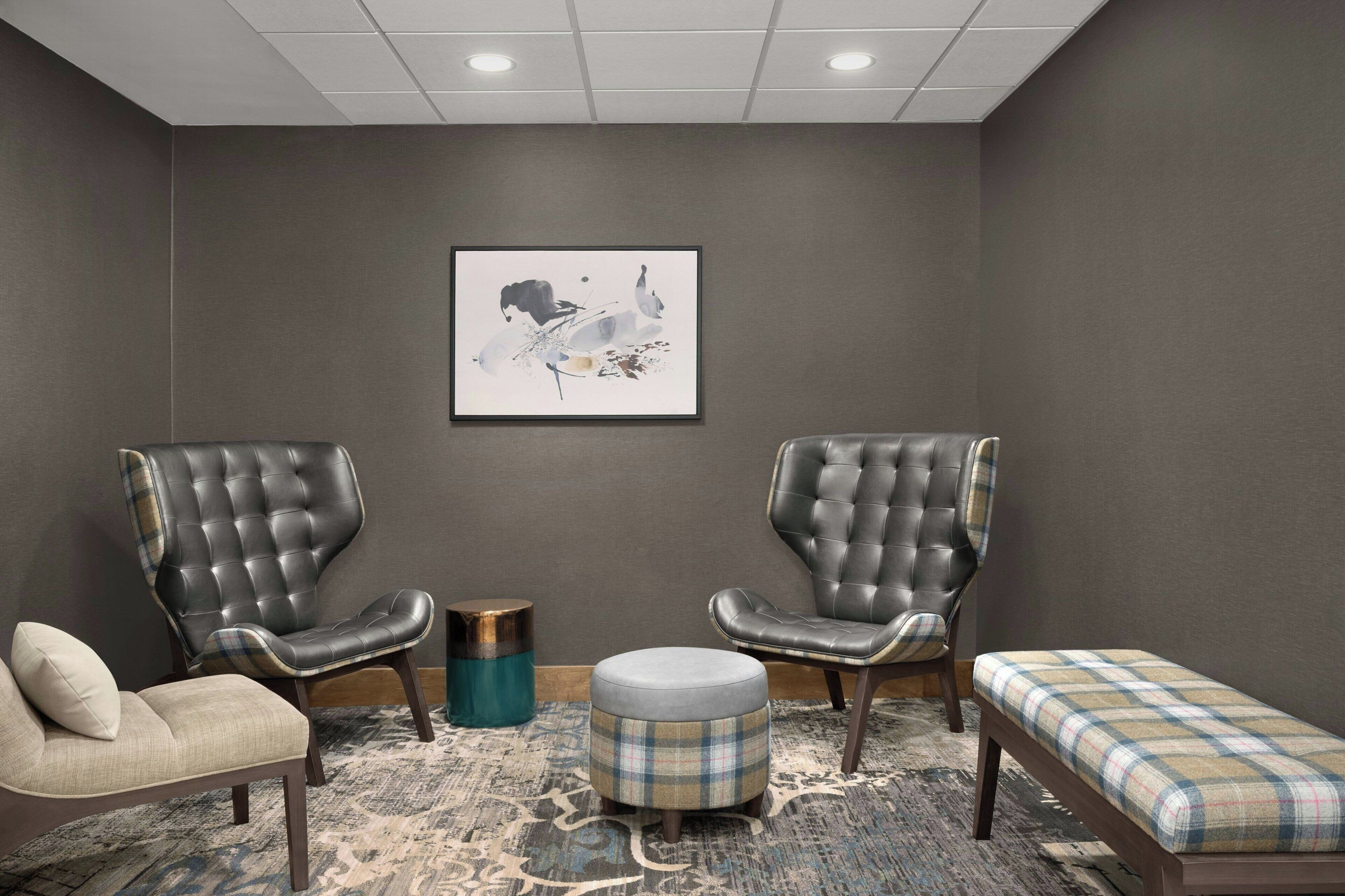 A room with two leather armchairs, a sofa, a small ottoman, and a bench with a plaid cushion.