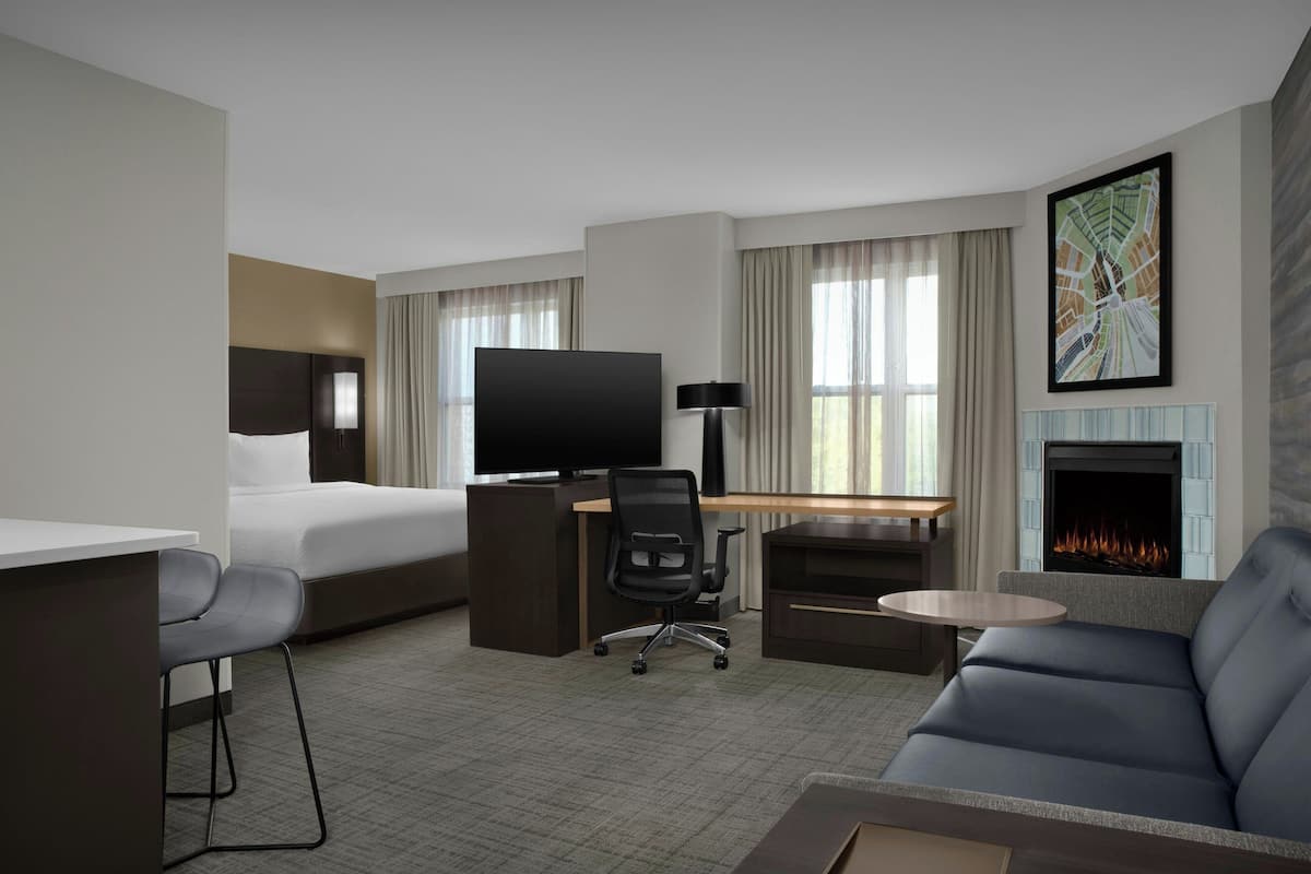 A hotel room with a bed, desk, TV, sofa, and fireplace.