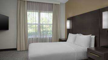 Quarto de hotel com cama grande, televisão, mesa de cabeceira e janela com cortinas.