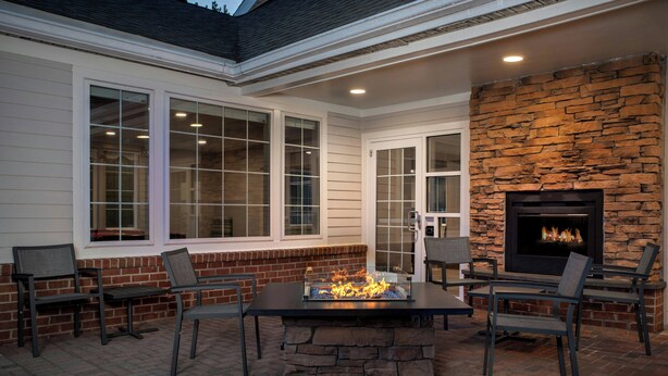 A patio with a stone fireplace, outdoor seating, and large windows. - Residence Inn by Marriott Arundel Mills BWI Airport (Hanover)