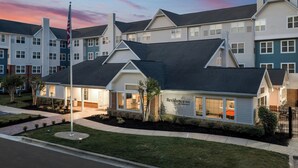 A multi-story hotel with a prominent American flag, a well-maintained lawn, and a clear sky. - Residence Inn by Marriott Arundel Mills BWI Airport (Hanover)