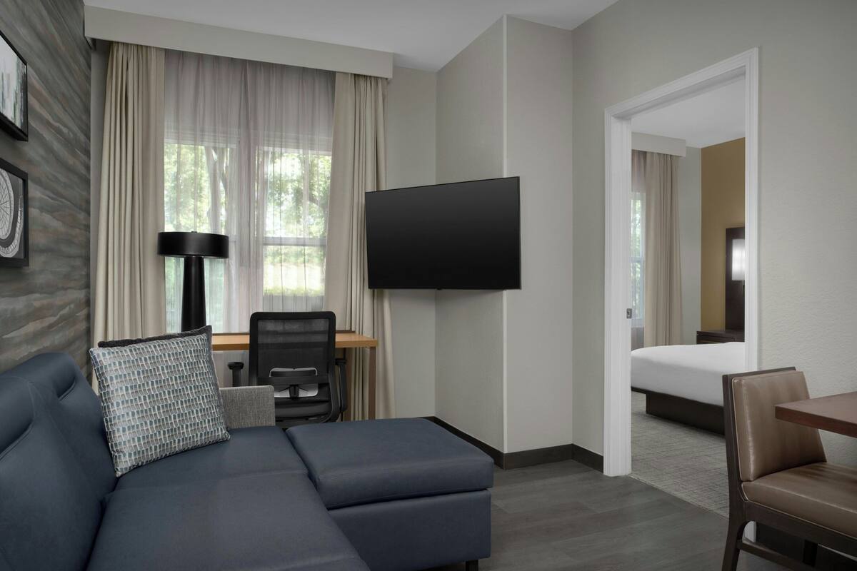 Hotelkamer met een bank, een bureau met stoel, een flatscreen televisie, een bed en een deur naar een andere kamer.