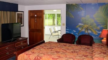 Habitación de hotel con cama, televisión, cómoda de madera y un mural de palmeras.