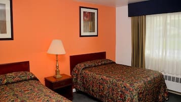 Una habitación de hotel con dos camas individuales, una mesita de noche con lámpara, una pared naranja, un cuadro enmarcado y una ventana con cortinas.