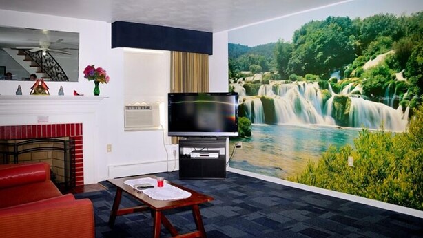 Una sala de estar con un televisor grande, una chimenea y un mural de una cascada.