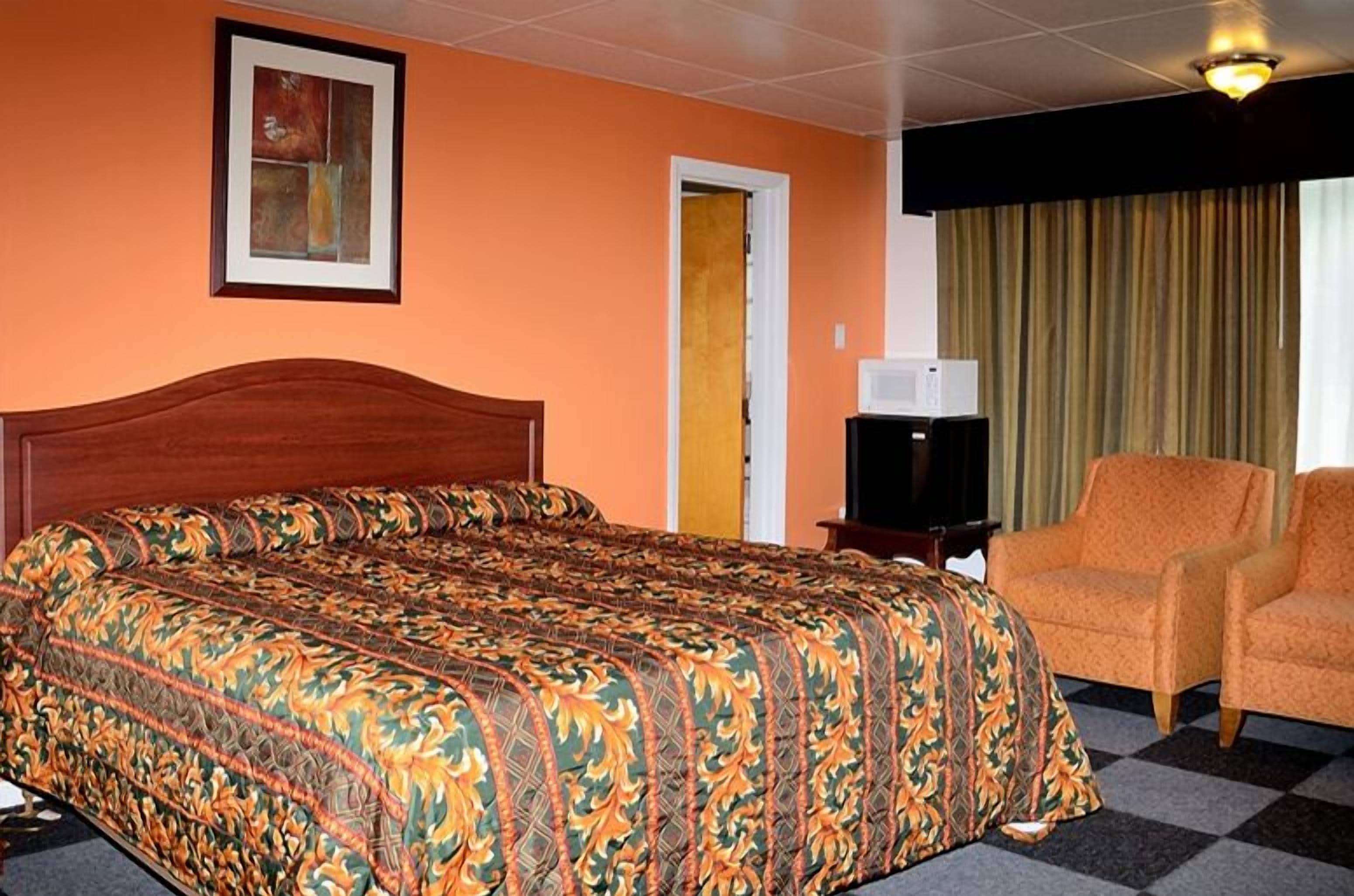 Una habitación de hotel con una cama grande, un televisor, un sillón naranja y una puerta.