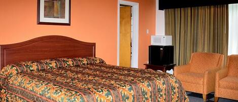 Una habitación de hotel con una cama grande, un televisor, un sillón naranja y una puerta.