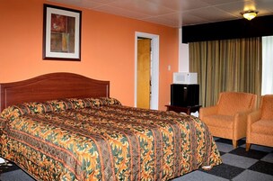 Una habitación de hotel con una cama grande, un televisor, un sillón naranja y una puerta.