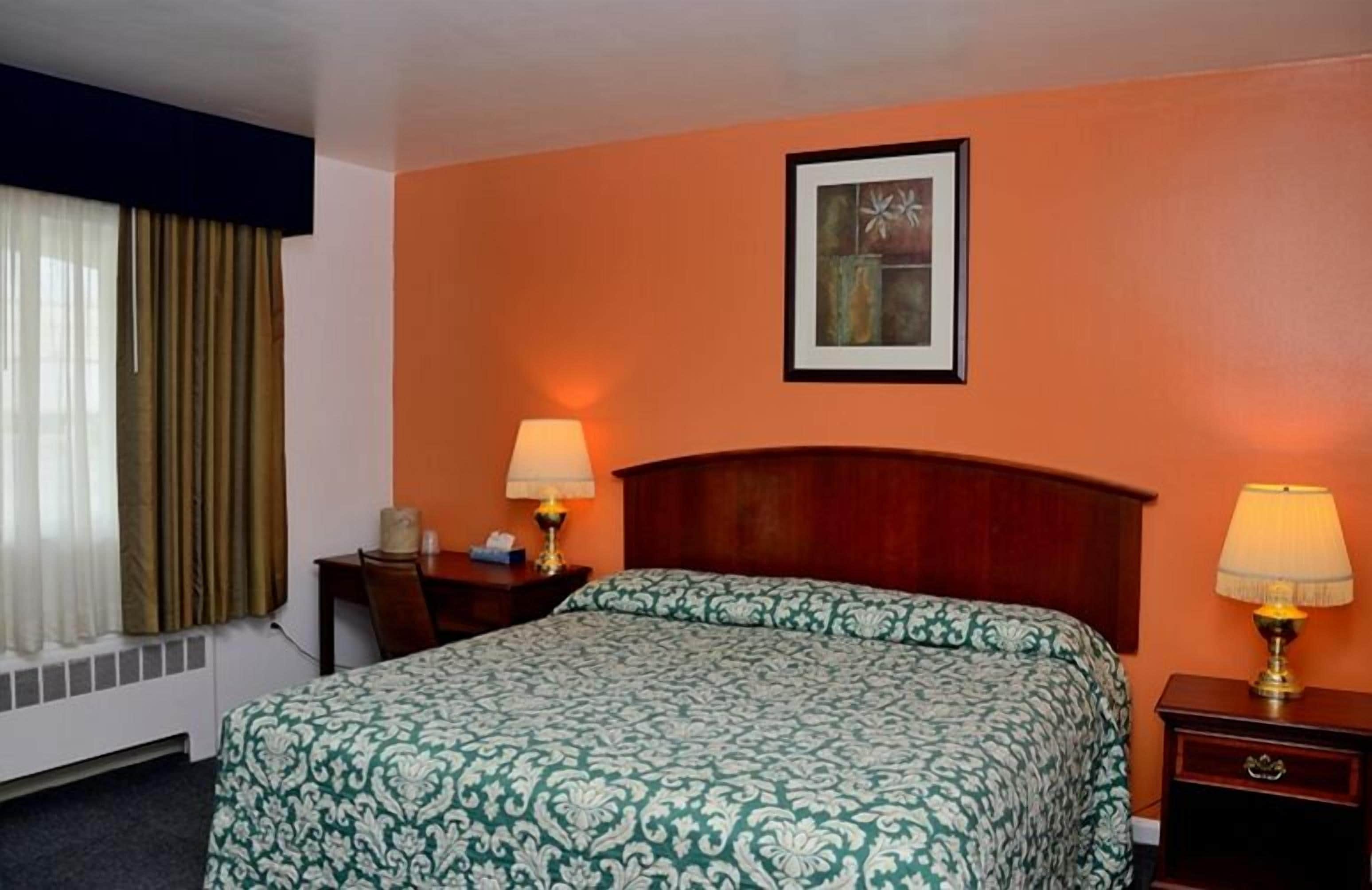 Hotelkamer met een bed, twee nachtkastjes met lampen, een lijst aan de muur en een raam met gordijnen.