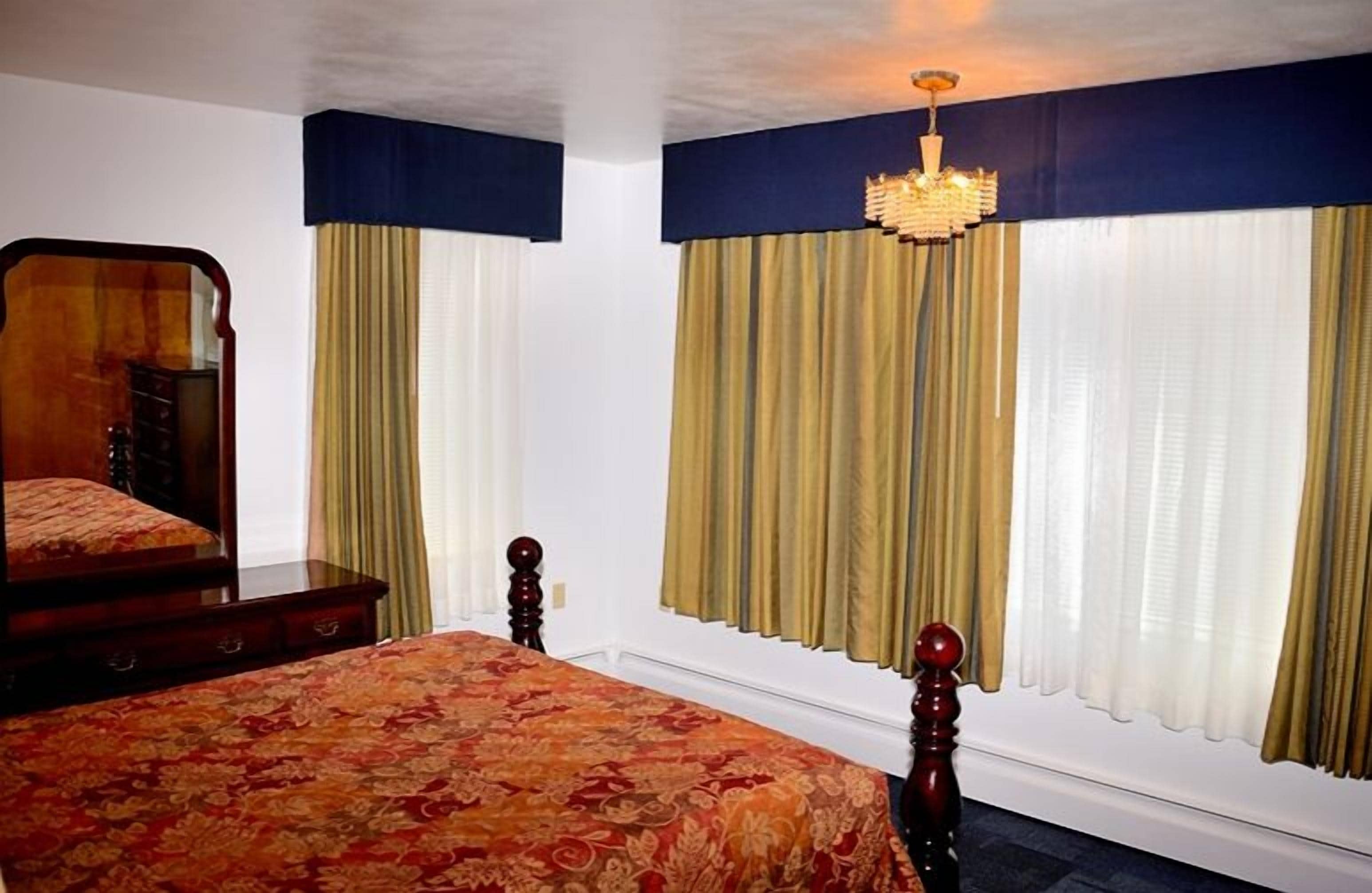 Une chambre à coucher avec un grand lit, une commode, un miroir et un lustre.