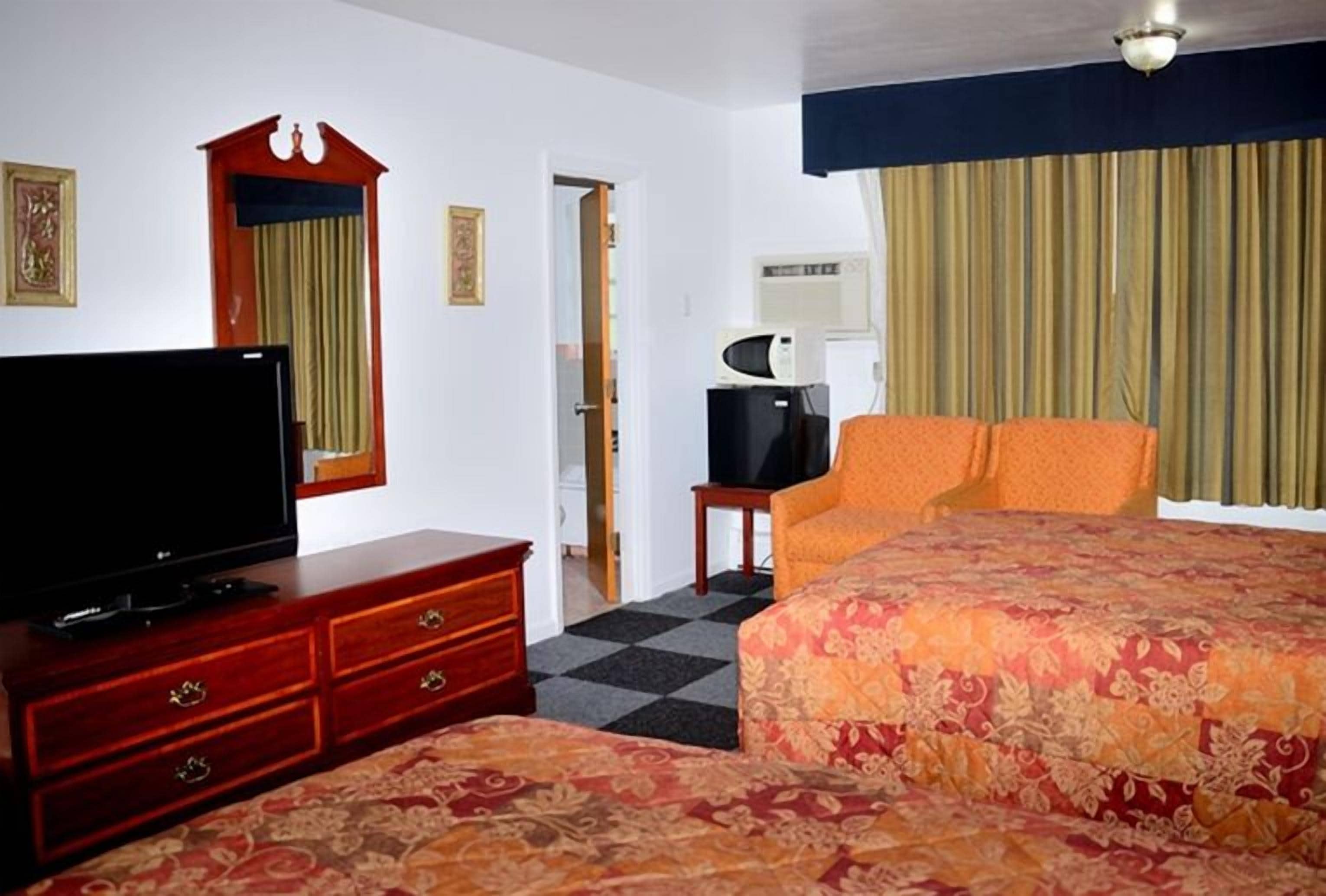 A hotel room with a bed, a television on a wooden dresser, a microwave, and a door leading to another room.