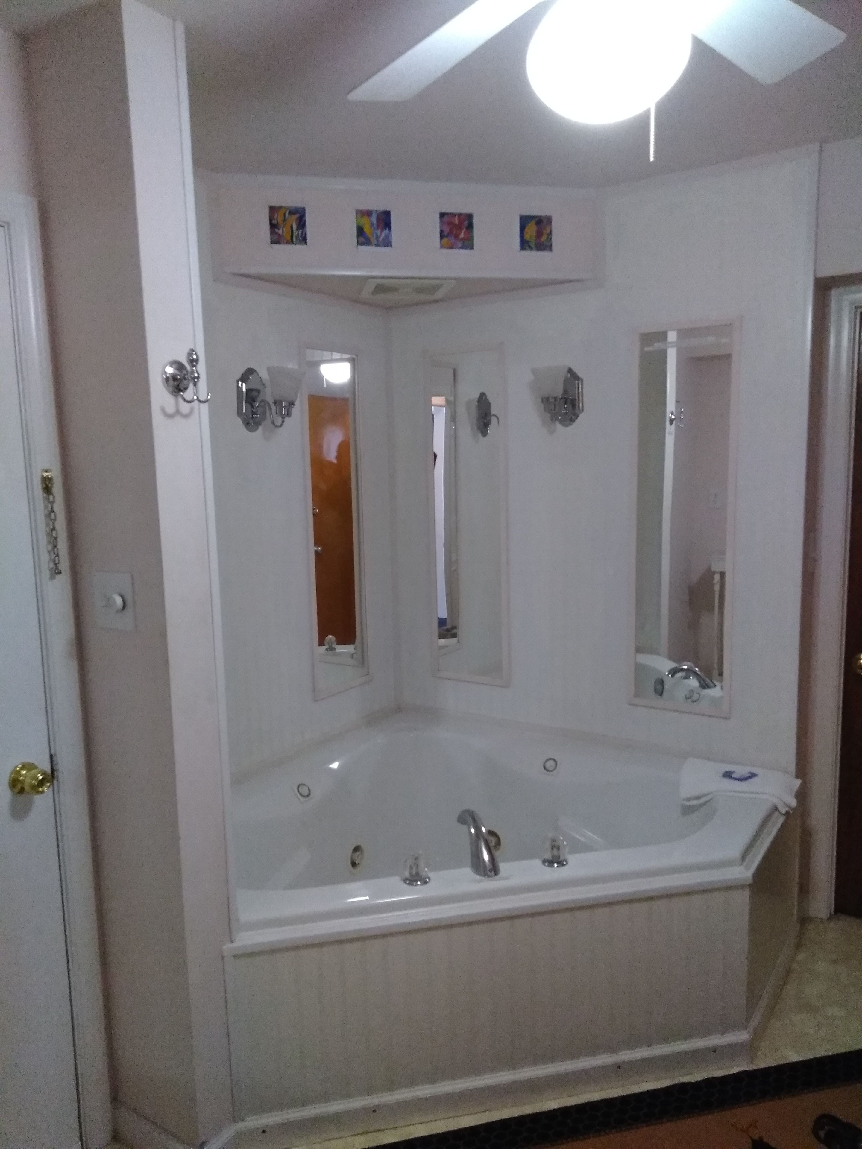 Une salle de bain dotée d’une grande baignoire, d’un ventilateur de plafond et de plusieurs miroirs.