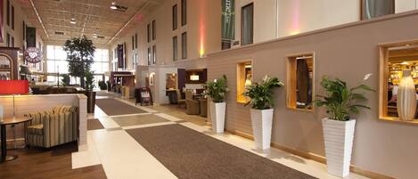 A spacious hotel lobby with a checkered floor, seating areas, and potted plants.