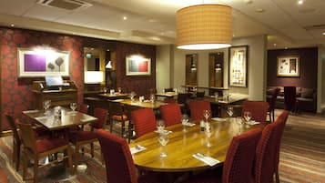 Un comedor de hotel con varias mesas y sillas, un mostrador de recepción y cuadros en las paredes.