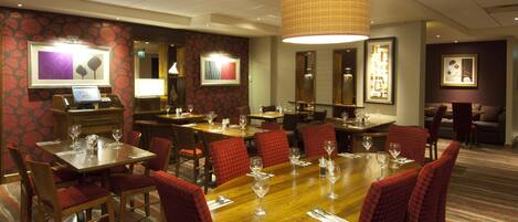 Une salle à manger d’hôtel avec plusieurs tables et chaises, un comptoir de réception et des œuvres d’art encadrées accrochées aux murs.