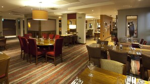 Un comedor de hotel con varias mesas y sillas, piso alfombrado e iluminación colgante.