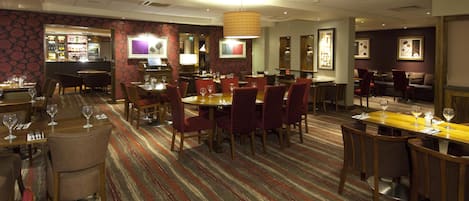 Un comedor de hotel con varias mesas y sillas, un bar y suelo alfombrado.