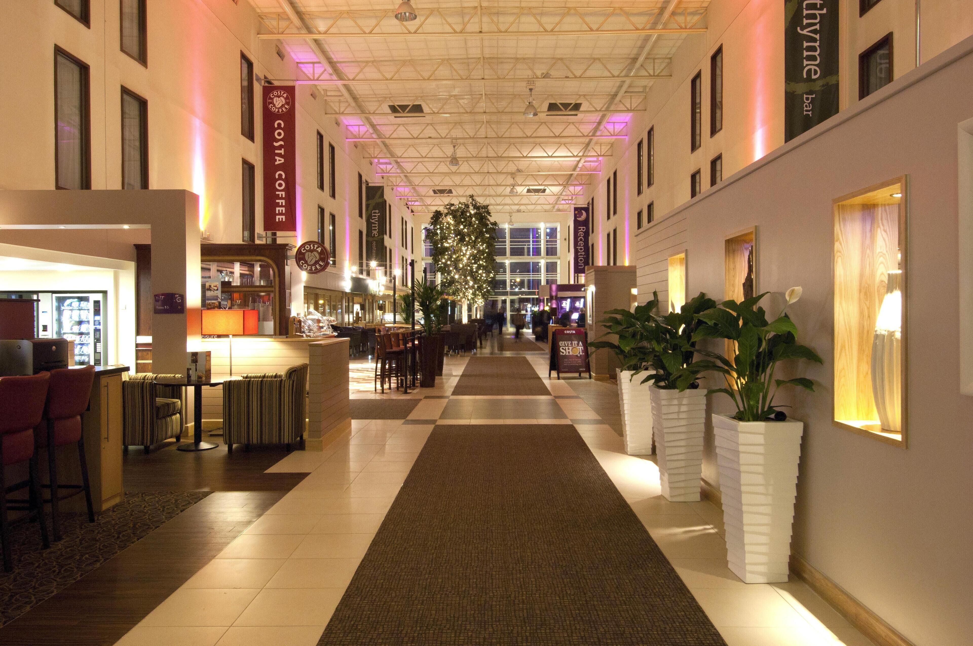 A hotel lobby with a reception desk, seating area, and a large plant.