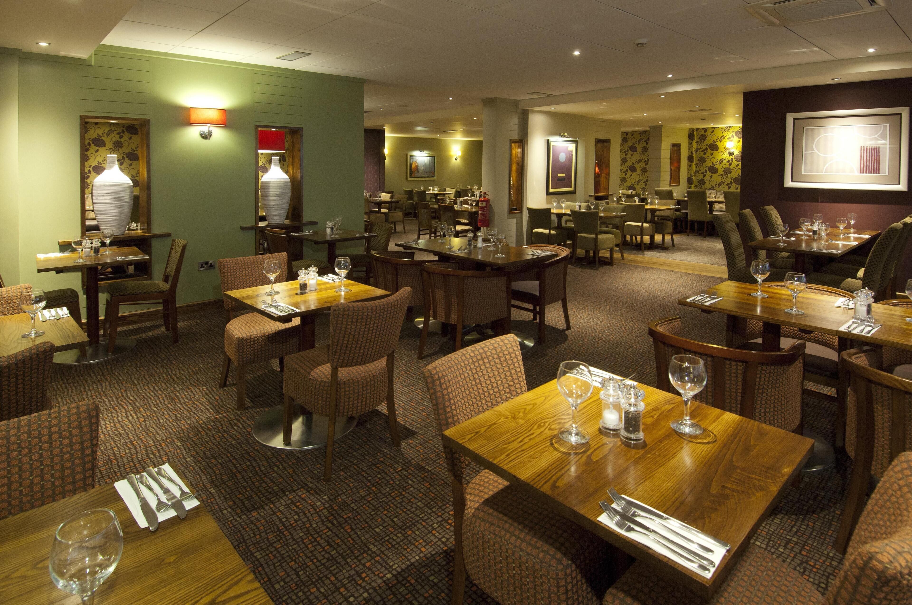 A hotel dining area with multiple tables and chairs, some with wine glasses and cutlery.