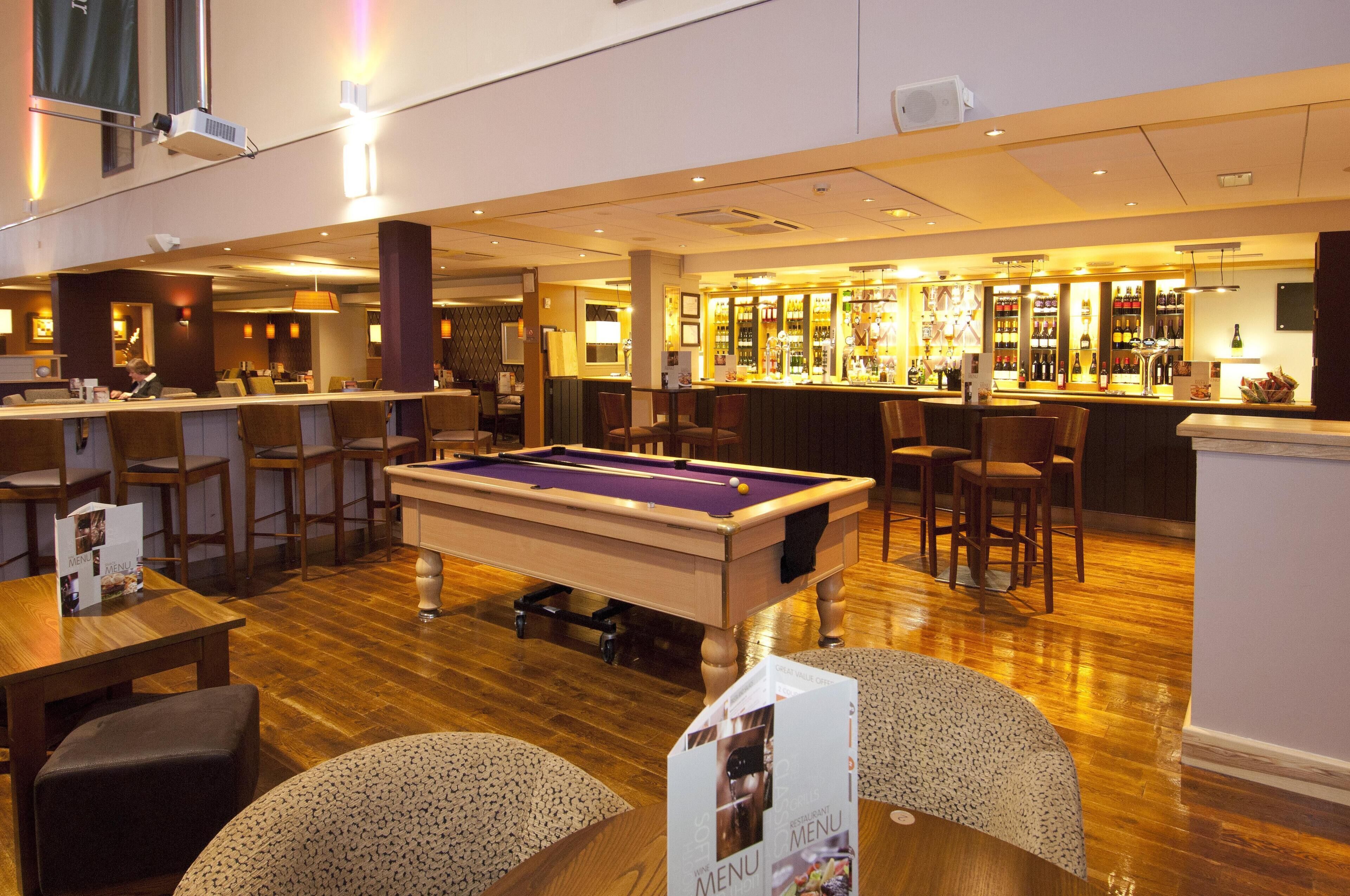 A billiards table in a hotel lobby with a bar and seating area.