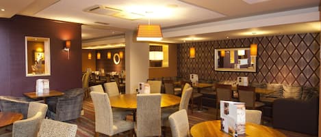 A hotel lobby with round tables, chairs, and a patterned wall.