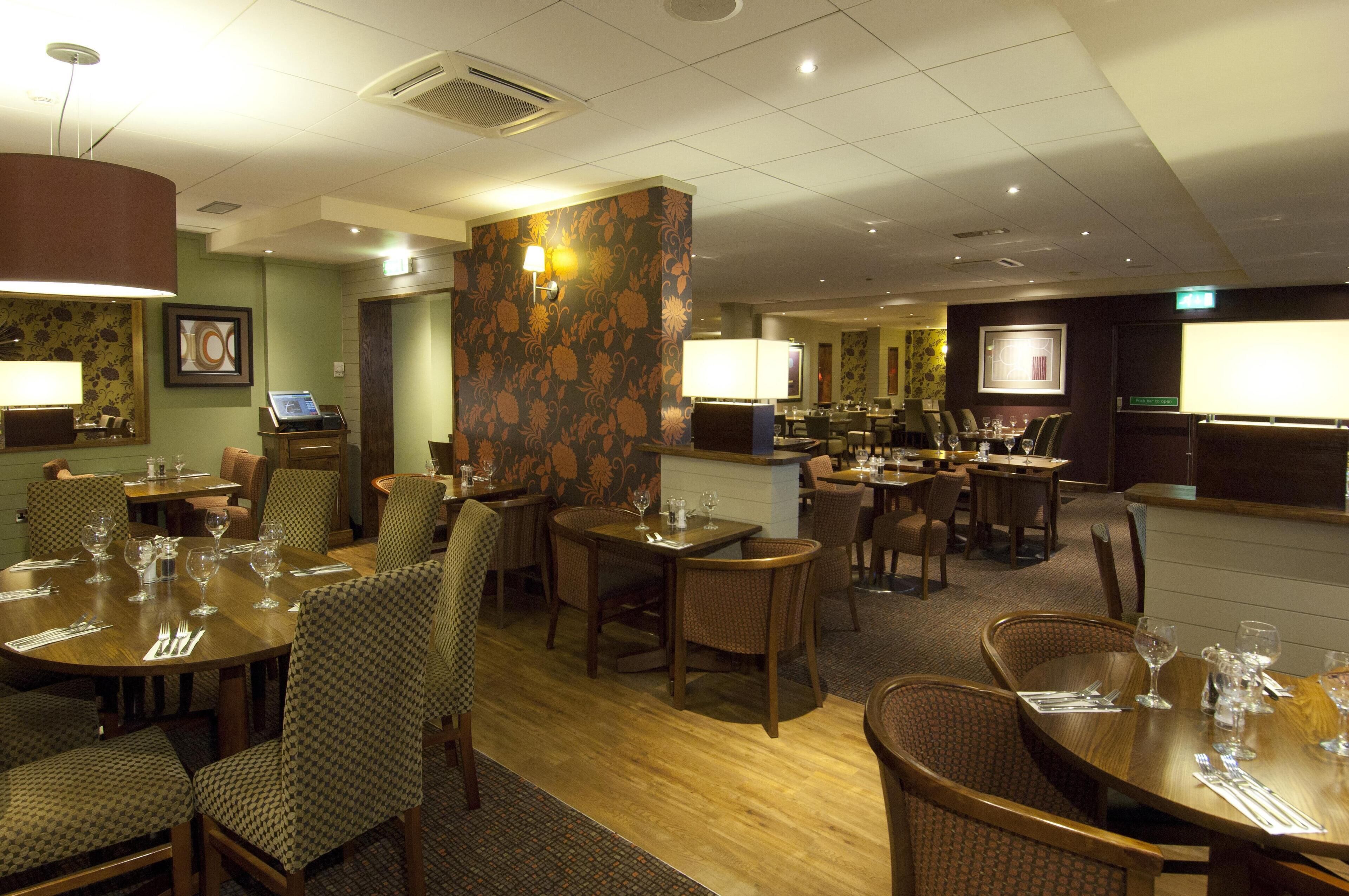 A hotel dining area with multiple tables and chairs, a reception desk, and a bar area.