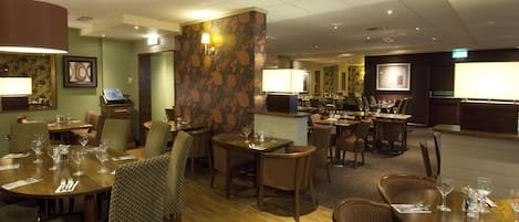 A hotel dining area with multiple tables and chairs, a reception desk, and a bar area.