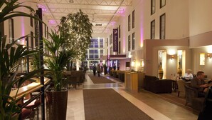 Un vestíbulo de hotel con una recepción, zonas de estar y una planta grande.