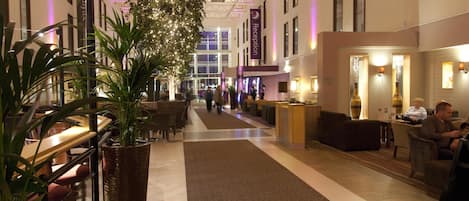 Eine Hotelhalle mit einer Rezeption, Sitzgelegenheiten und einer großen Pflanze.