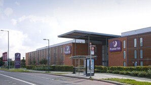 Ett Premier Inn-hotell med en modern fasad i tegel, ett överbyggt busshållplats och en klar himmel.