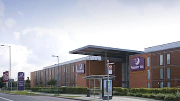 A Premier Inn hotel with a modern brick facade, a covered bus stop, and a clear sky.