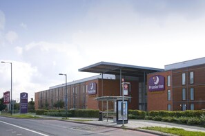 A Premier Inn hotel with a modern brick facade, a covered bus stop, and a clear sky. - Premier Inn London Heathrow Airport T2 & T3 - Bath Road (Hounslow)